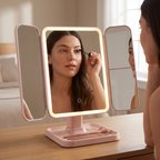 Pink trifold vanity mirror in use, applying mascara at a dressing table